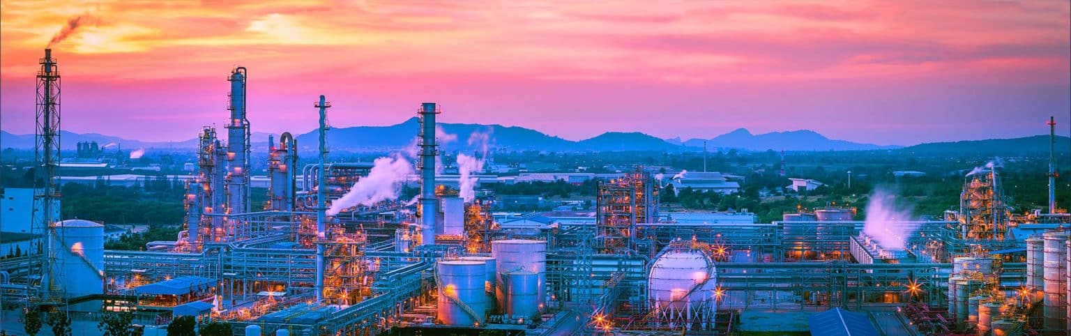 A sprawling, chemical production facility, with storage tanks and towers interconnected by a large network of pipes.