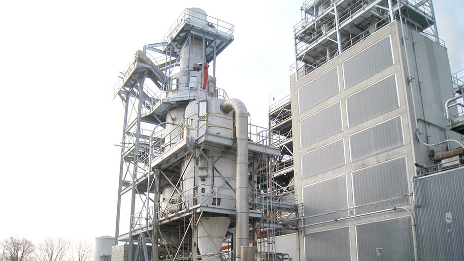 A large dust collector unit sits outside of an industrial plant. A set of metal stairs sits on the outside of the unit.